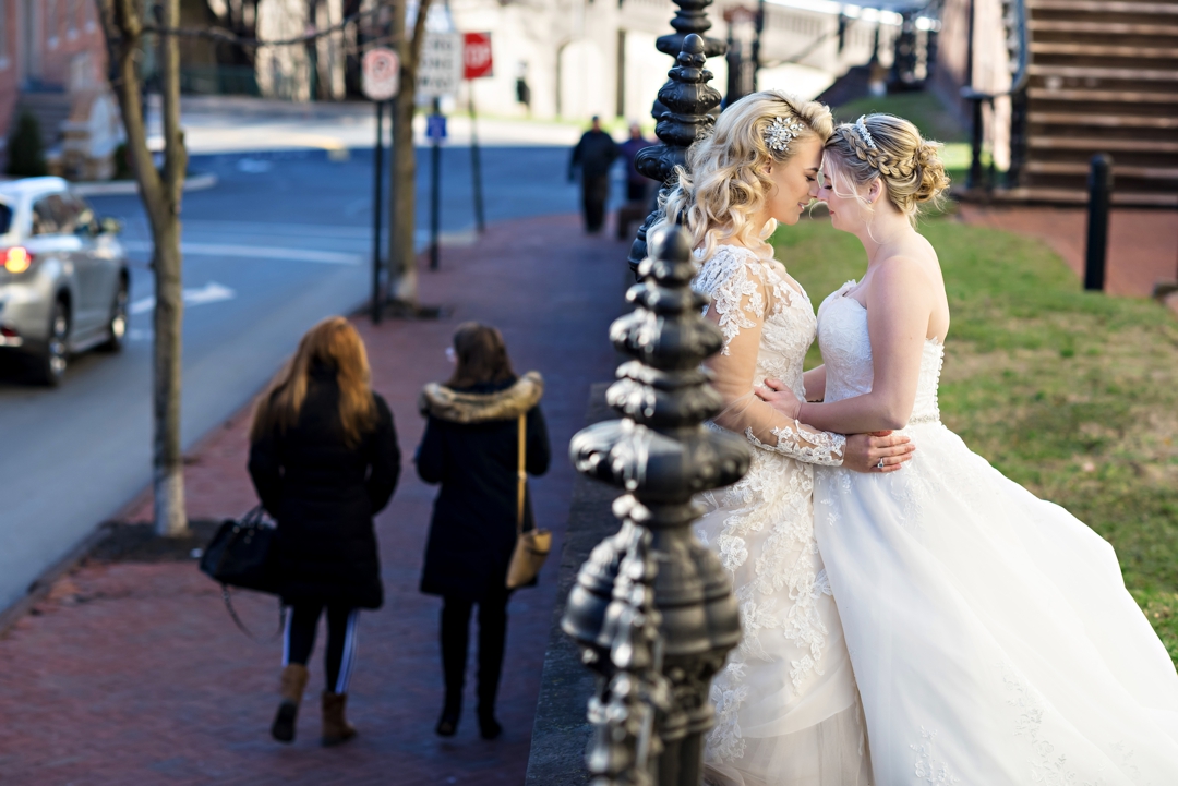 Two brides hug against a fence in Bethlehem PA before their Wedding.
