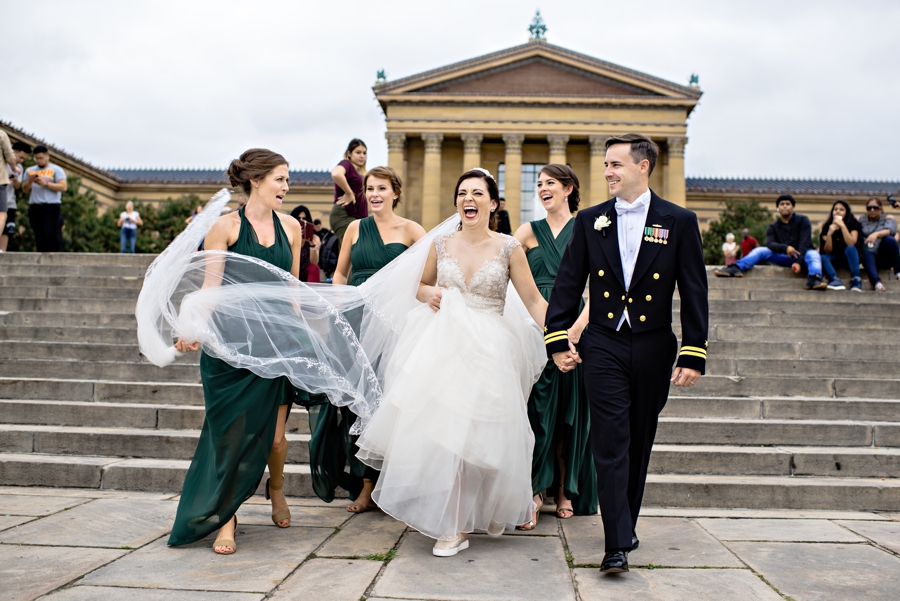 A wedding party laugh and walk down the rocky steps at the Philadelphia Art Museum.