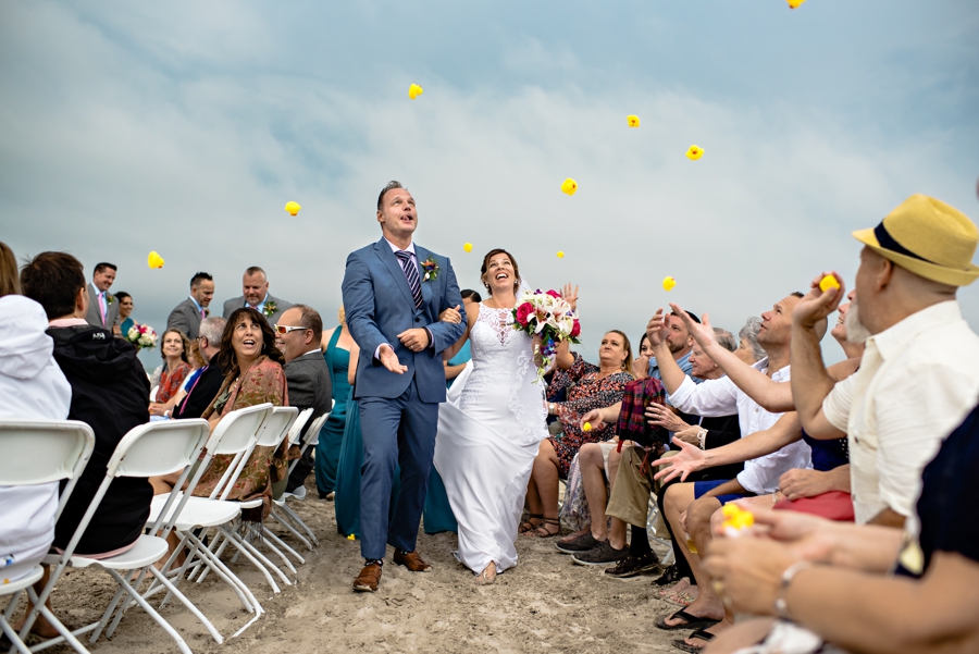 A bride and groom exit thier ceremony on the beach in cape may while their guests throw rubber ducks.