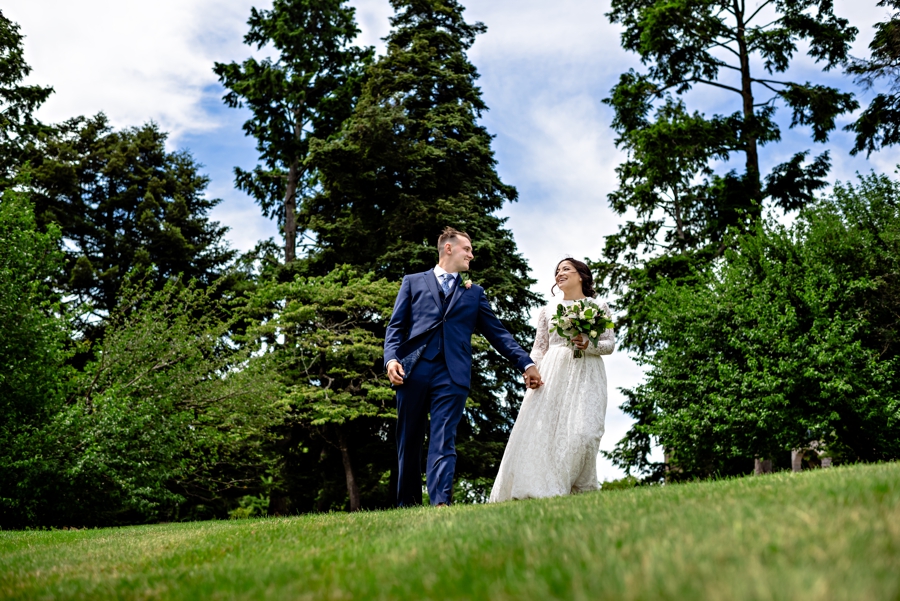 A newly married couple hold hands a laugh while walking in the grass at Cairnwood Estate.