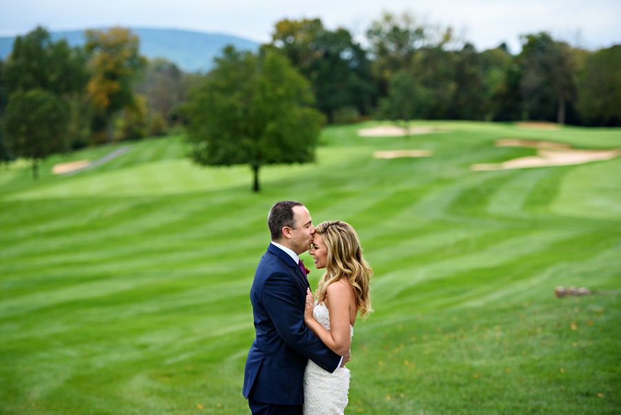 A groom holds his bride and kisses her forhead on the golf course at Lehigh Country Club.