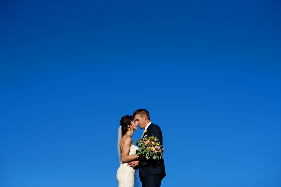 A newly married couple kiss under a blue sky at their Stoltzfus Homestead Wedding.