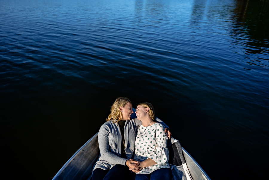 A same sex couple hold hands in a boat on a lake during their engagement session.
