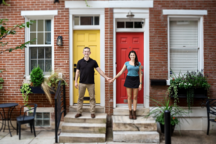 A man and woman hold hands in front of Philly row homes for their engagement session.