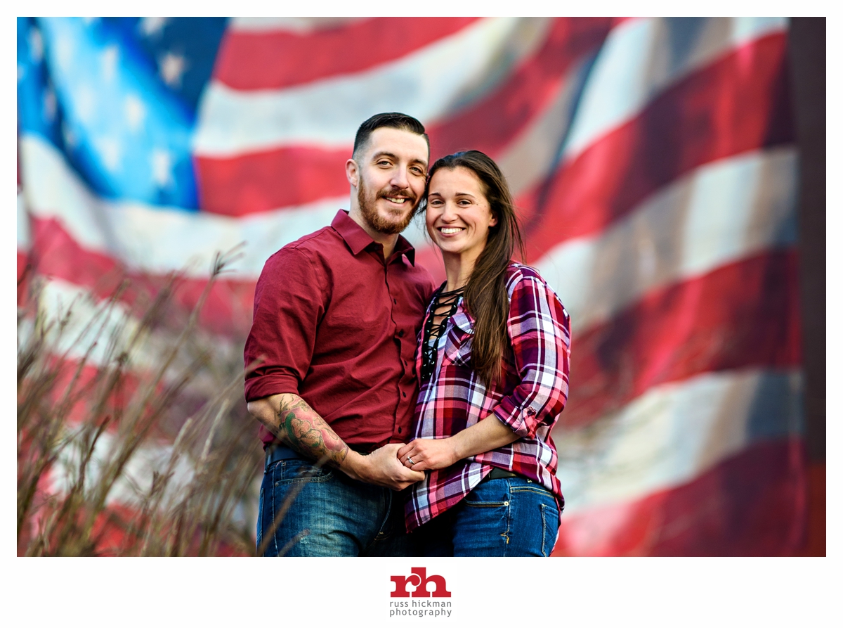 An army couple come to Philadelphia for their engagement session and hug in front of an American flag mural.