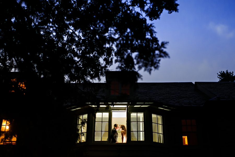 A newly married couple sit in the window of a mansion in merion station PA at sunset after thier wedding.