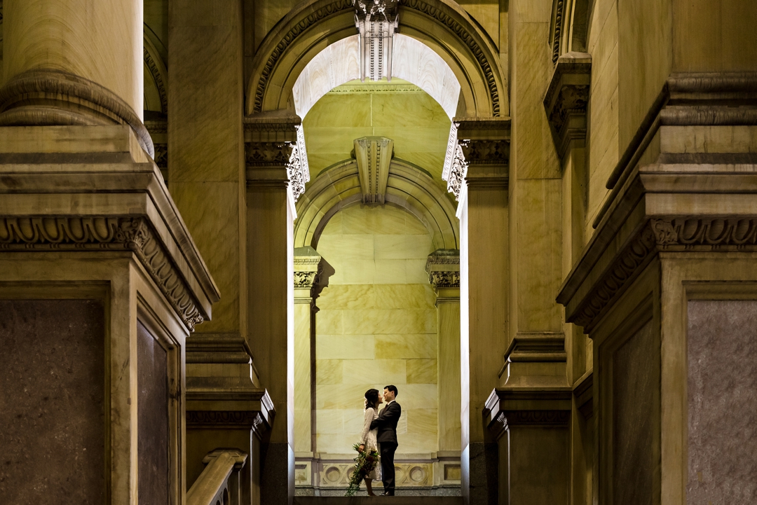 A bride leans into her groom for a kiss under the arches of city hall in Philadelphia.