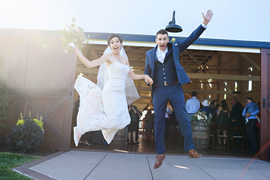 A bride and Groom jump in the air coming out of the barn after the wedding ceremony at Stoltzfus Homestead and Gardens.