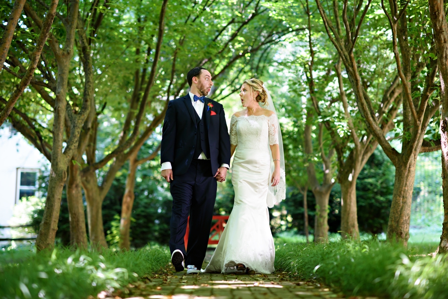 A married couple walk along a tree lined walkway and make silly faces after their wedding at Appleford Esatates in Villanova, PA.