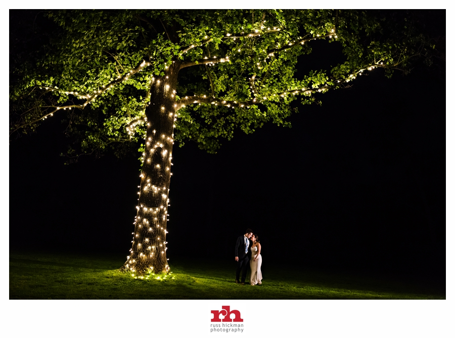 A Bride and Groom take a walk at night under a tree filled with lights at their Anthony Wayne House Wedding.