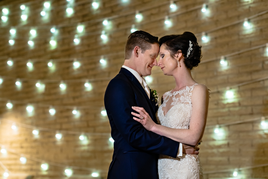 A couple hold each other in front of a wall of lights after their wedding ceremony.